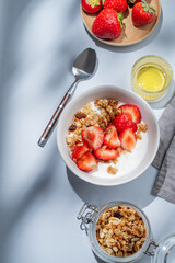 Granola or muesli with natural greek yogurt, strawberry and honey in a bowl on a blue background