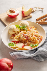 Peach crumble or cobbler with vanilla ice cream scoops and cinnamon on a plate on a light background