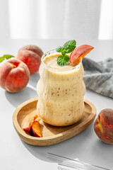 Smoothie with peach and banana in a glass on a wooden board on a white table near window