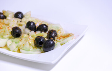 A white plate with a salad of cucumbers and olives
