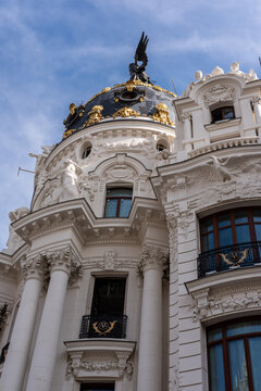 View of the Metropolis Building's ornate facade, its white stone contrasting against the blue sky, framed by intricate architectural details, Madrid, Spain.