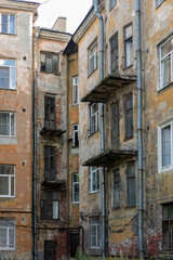 The weathered and decaying facade of an old apartment building with balconies and drainage pipes