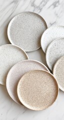 Stack of speckled, earthy-toned ceramic plates on a marble surface. Natural light illuminates the scene