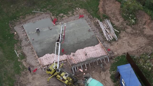Aerial drone view of construction crew pouring concrete to build base of house.