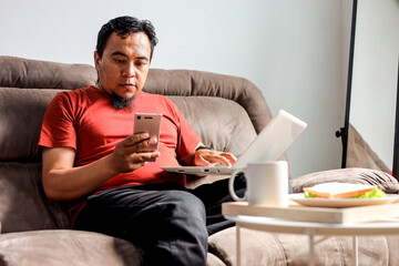 Asian Adult Male Using Laptop and Smartphone at the Same Time at Home