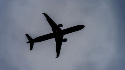 A large jet plane is flying through a cloudy sky. The plane is almost completely black, with only its tail and wings visible. The sky is dark and gloomy, with the clouds looming overhead