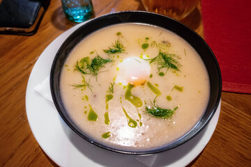 Dill soup with poached egg and oil in bowl on table.