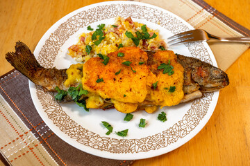 Breaded trout with scrambled egg and ham, sprinkled with green parsley.