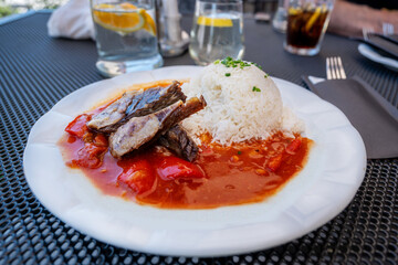 Sliced boiled beef in gypsy sauce with rice on plate on restaurant table.