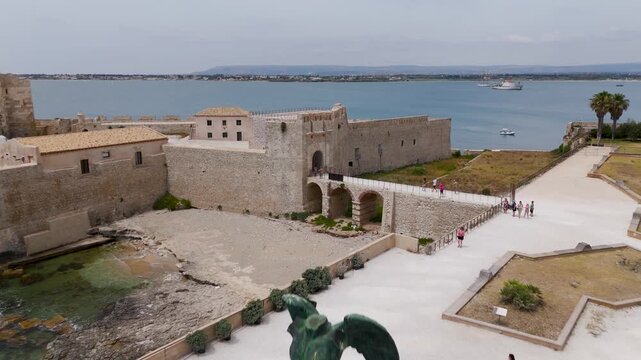 Aerial Drone Shot Of Mitoraj Sculpture And Ortigia Island In Syracuse, Sicily, Italy On A Bright Summer Day.