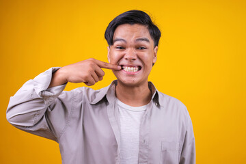 Asian Guy Using Index Finger Touching The Corners of Mouth While Smiling Broadly Showing Teeth