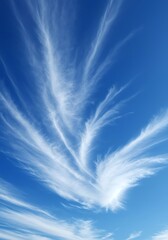 Wispy cirrus clouds stretch across a clear blue sky in a vertical shot