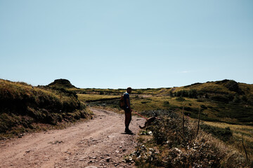 Man with a backpack walking a German Shepherd on a mountain trail in Stara Planina, Serbia. Rocky path under clear sky, summer hiking landscape