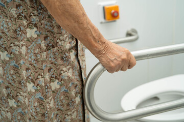 Asian elderly woman patient use toilet support rail in bathroom.