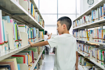 A young boy is seen selecting books from the shelves in a well-lit library, engaging in a learning...