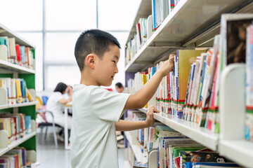 A young boy is choosing books from the shelves in a library, engaging in an educational activity of selecting reading materials.