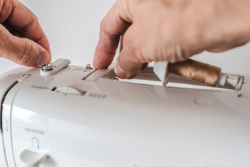 Male tailor preparing modern sewing machine at workplace, closeup photo. Male hands threading sewing machine through tension discs, step-by-step process