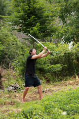 Man in black shirt waving Japanese traditional sword katana outdoors