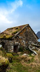 An aged stone structure, weathered and overgrown with moss and grass, rests on a grassy hillside under a partly cloudy sky.