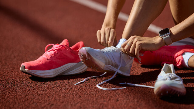 Close-up runner tying spikes on athletics track before hurdles race. Concept of preparation, psychological readiness, focus, and discipline in overcoming barriers.