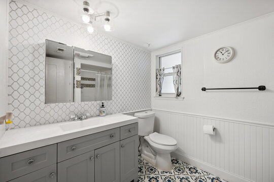 A bathroom featuring a sink, toilet, mirror, and a clock on the wall