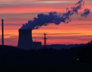Fototapeta premium Silhouette of industrial power plant at sunset, emitting smoke against a vibrant sky