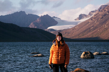 A young woman by a mountain lake overlooking a snow-covered peak. Camping and hiking in the mountains in summer