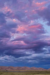 Dusk paints the sky with vibrant pinks and purples above a grassy plain and sand dunes