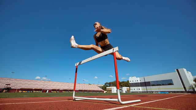 Female hurdler powerful leap above hurdle against clear sky. Concept of freedom, empowerment, sport challenge, mental resilience, and professional athletic success.