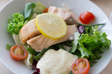 A close-up of a salmon salad with lettuce, cherry tomatoes, and a lemon slice, with a creamy sauce...