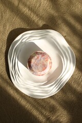 Top View on Elegant Round Soap on Textured White Plate, Minimalist Still Life with Soft Shadows.
