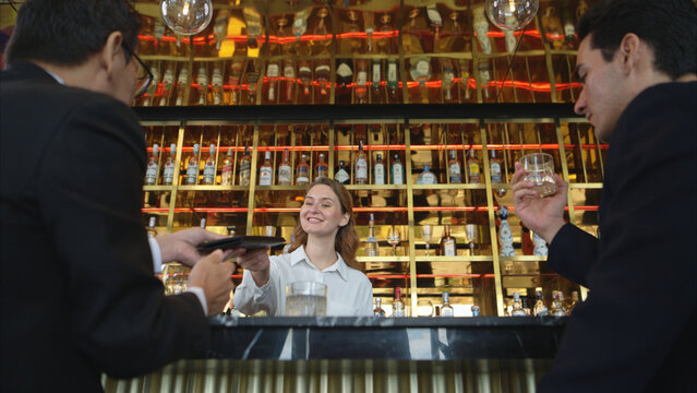 Smiling bartender serving drinks to customers at a modern bar