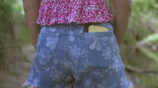 Woman putting mobile phone into back pocket of denim shorts