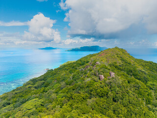 Aerial view of Praslin Island, Seychelles, featuring lush green hills, tropical coastline, and calm...