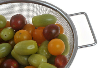 Tomates cerises de différentes couleurs et saveurs dans une passoire en gros plan sur fond blanc