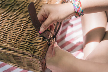 Woman opening wicker picnic basket on checkered blanket by river