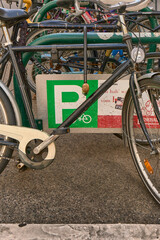 Close-up of a bicycle frame parked at a green bicycle parking sign showing the &ldquo;P&rdquo; symbol, with numerous other bicycles tightly parked in the blurred background.