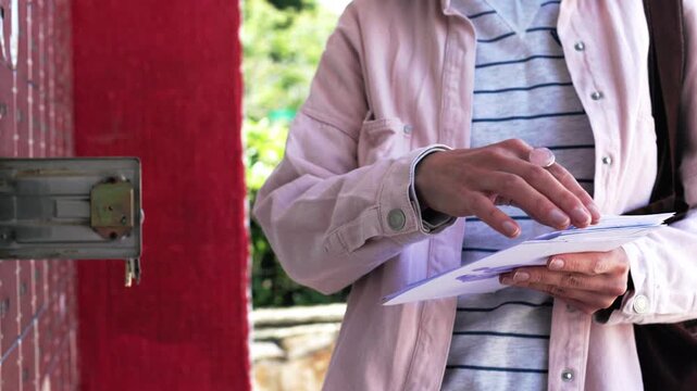 Stylish young girl stands at the mailbox with envelopes in her hands. Woman holds a stack of envelopes in her hands. Girl checks mail.