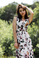 A girl in a light flower dress stands in a field on a stump. Around her is green grass with yellow...