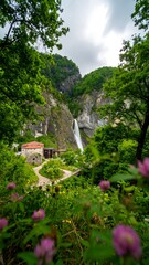 A verdant landscape showcases a cascading waterfall, a rustic building nestled amongst lush greenery, and vibrant wildflowers in the foreground.