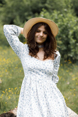 Girl in a white dress and hat on a green field in summer.