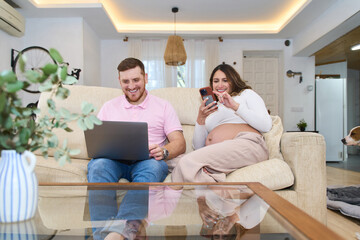 Happy couple using laptop and smartphone relaxing on sofa in living room