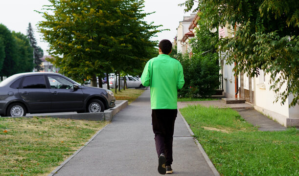 Man jogging on sidewalk in urban area during early morning hours surrounded by trees and parked cars - Powered by Adobe