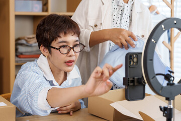 Senior asian female writes checklist while adult daughter prepares package with branded box, teamwork managing ecommerce family shop, small fashion business collaboration in creative boutique