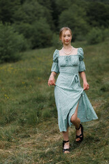 Woman in a long turquoise dress with a slit and beads on her neck, in a field