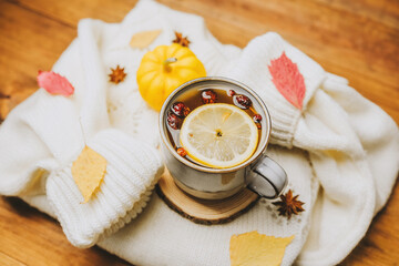 Warm drink with lemon and berries, soft white sweater, autumn leaves, and small pumpkin on wooden...