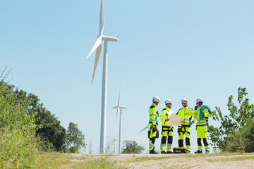 Team of engineers inspecting and planning maintenance at wind turbine power site. They discuss and...