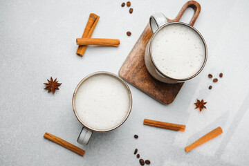 Two warm drinks with foam and spices, cinnamon sticks, star anise, coffee beans on grey surface.