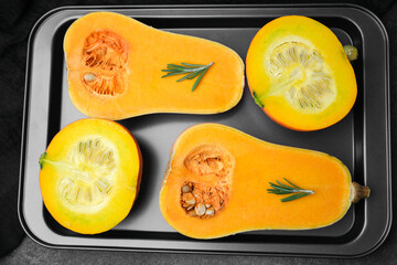Halved orange squash with rosemary on a metal tray, prepared for cooking