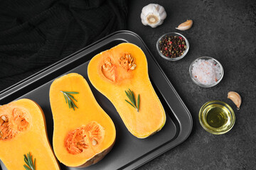 Halved butternut squash with rosemary on baking tray, garlic, salt, peppercorns, oil